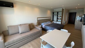 Una habitación de hotel moderna con sofá, cama, mesa de comedor y kitchenette.