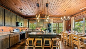 A spacious kitchen with wooden cabinets, a central island with stools, and a dining area with wooden tables and chairs. - Ultimate Mountain Getaway Pickleball & Basketball Courts Games Hot Tub Sleeps 20 (Sevierville)