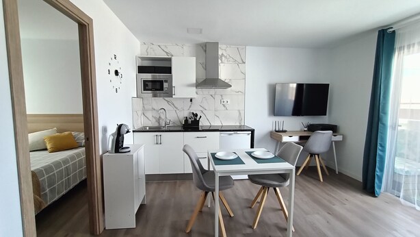 A modern kitchen with a microwave, stove, and sink, a dining area with a table and chairs, and a TV mounted on the wall. - Self-contained apartment, The Greey's House F (El Calero)