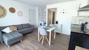 A compact living space with a grey sofa, a dining table with chairs, a washing machine, and a kitchen area with a sink and utensils. - Self-contained apartment, The Greey's House F (El Calero)