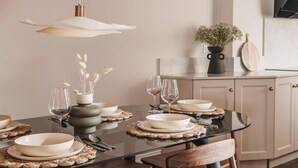A dining table set with plates, bowls, and wine glasses, with a vase of flowers and a wooden board on the counter. - Springfield-Windermere (Windermere)