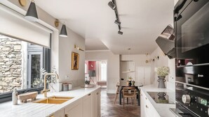 A modern kitchen with a large island, built-in oven, and a stone wall. - Springfield-Windermere (Windermere)
