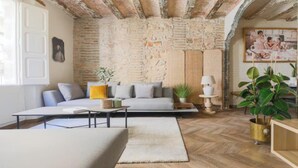 A cozy living room with a stone wall, a sofa, a coffee table, and a large plant.