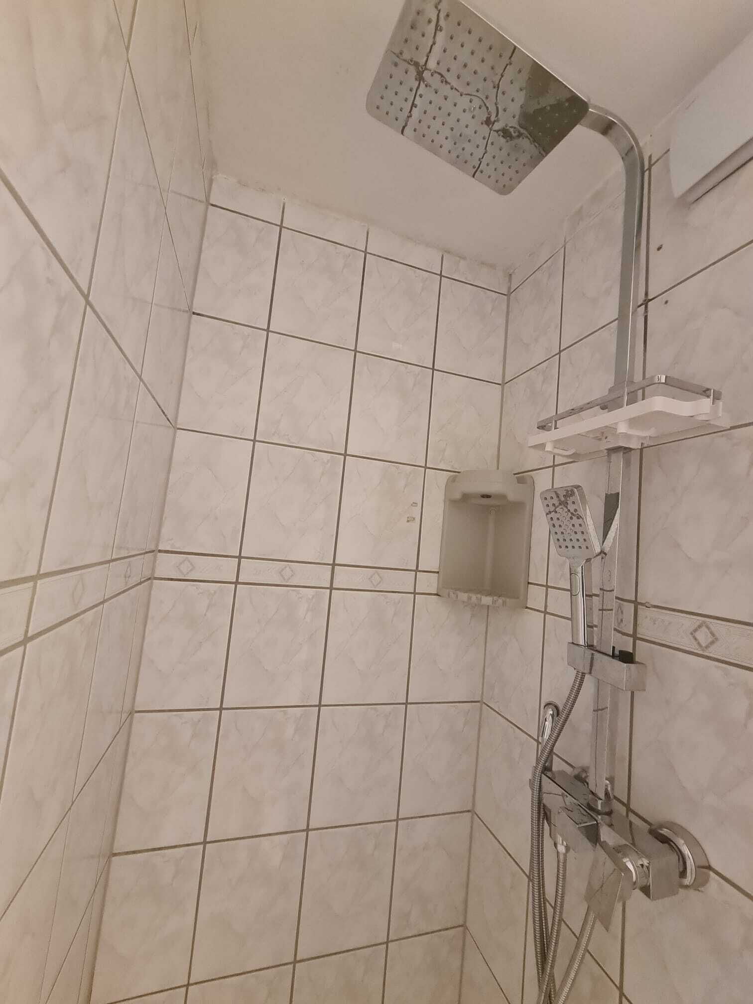 A shower area with a handheld showerhead, a wall-mounted control panel, and a small shelf.