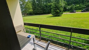 A balcony with a view of a green lawn and trees, a table with a blue object, and a railing. - Pause Nature 30N _ living in nature in peace and quiet (Kelmis)
