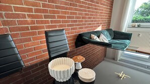 A modern living space with a brick wall, a glass table, black chairs, and a green sofa with cushions. - Schönblick House B6 · Large Panoramic Terrace (Schöfweg)