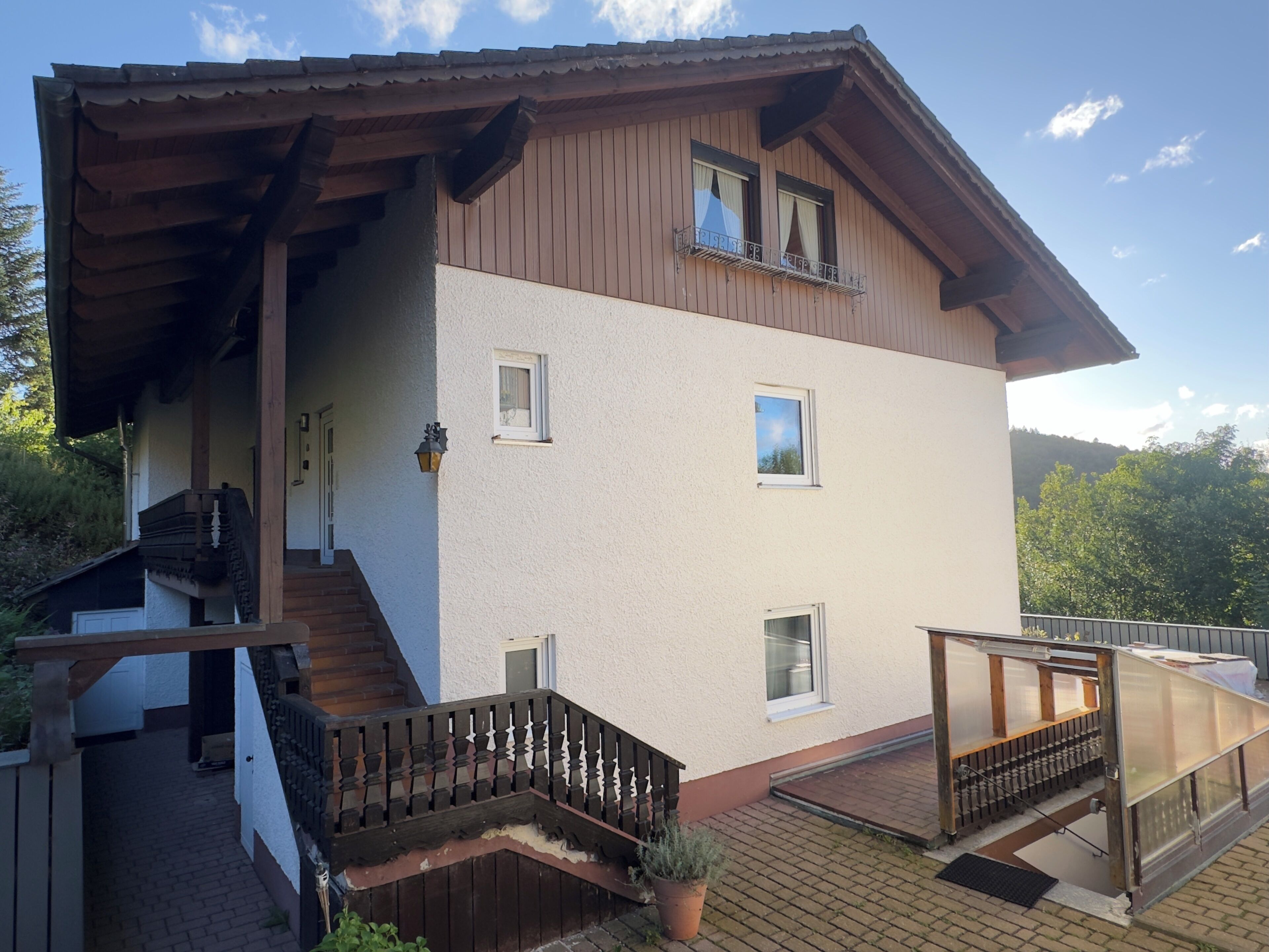 A two-story house with a wooden deck, a staircase, and a small balcony.