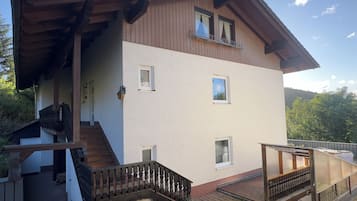 A two-story house with a wooden deck, a staircase, and a small balcony.