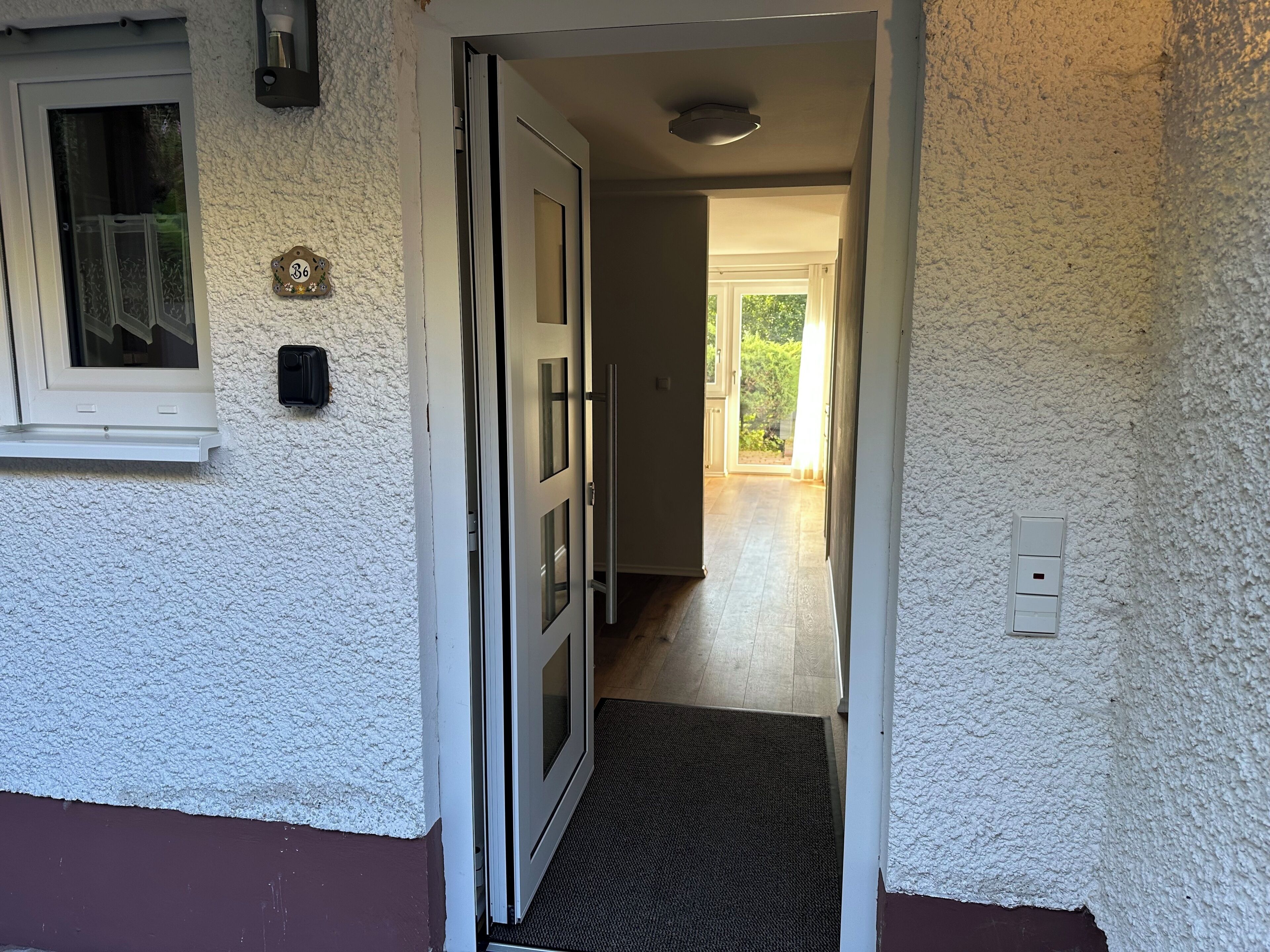 Passatge que condueix a una habitació amb una porta, una finestra amb cortina i una làmpada fixada a la paret.