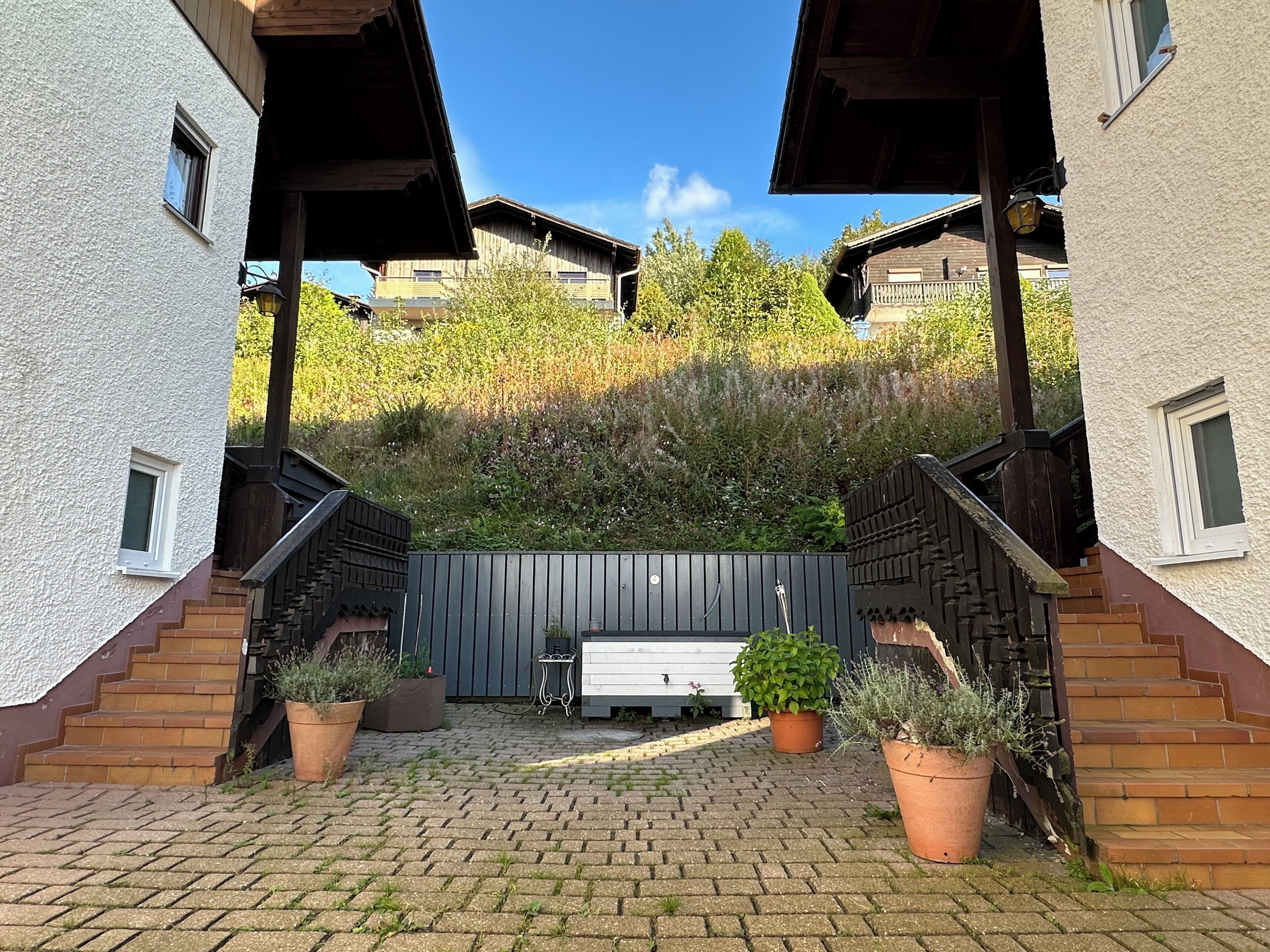 Ein Innenhof mit gepflastertem Weg, einer hölzernen Bank und Blumentöpfen.