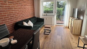 A cozy living room with a brick wall, a dark green sofa, a wooden coffee table, and a TV on a wooden cabinet. - Schönblick House B6 · Large Panoramic Terrace (Schöfweg)