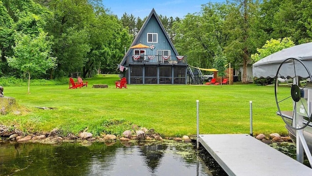 Ein Haus mit einer Terrasse, umgeben von einem Rasen und einem Teich.