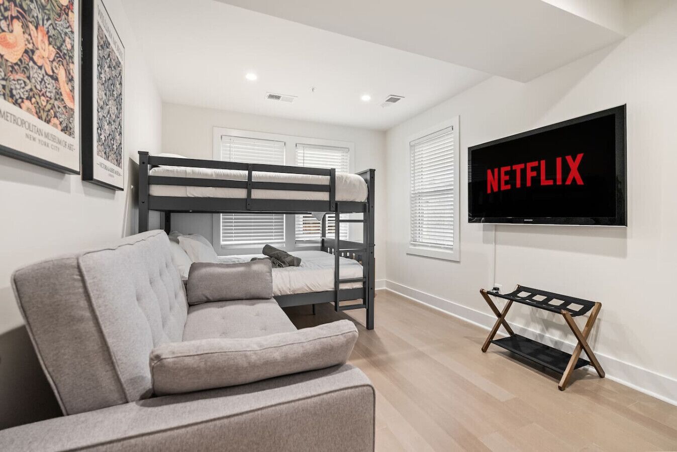 A modern room with bunk beds, a grey sofa, a flat-screen TV, and framed pictures on the wall.