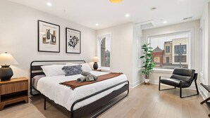 A modern bedroom with a bed, bedside lamps, a city view, and artwork on the wall. - Columbia Heights 5BR · Sleeps 14 · Whole House (Washington)