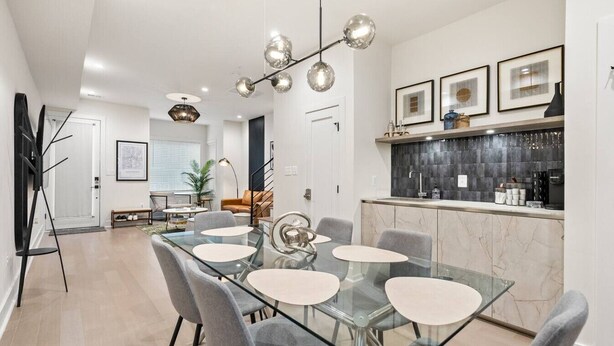 A modern kitchen with a marble countertop, a dining area with a glass table and grey chairs, and a staircase leading to another level. - Columbia Heights 5BR · Sleeps 14 · Whole House (Washington)