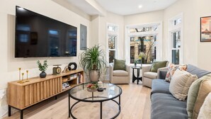 A modern living room with a flat-screen TV, a wooden console table, a glass coffee table, a grey sofa, and two armchairs.