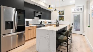 A modern kitchen with a stainless steel refrigerator, a built-in oven, and a marble island with bar stools.