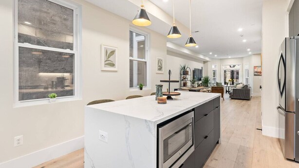 A modern kitchen with a large island, pendant lights, and a built-in oven.