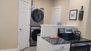 A compact kitchen with a built-in oven, a microwave, and a stovetop. There are two white cabinets with drawers, a countertop with a kettle, and a wall-mounted spice rack. - 1895 meets 2025 Townhouse in Urban Hamilton (Hamilton)