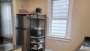 A kitchen with a stainless steel refrigerator, a microwave, and a black shelving unit with dishes and glasses. - 1895 meets 2025 Townhouse in Urban Hamilton (Hamilton)