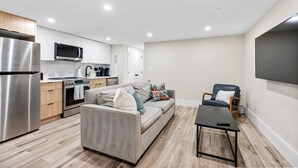 Un appartement moderne doté d’une kitchenette, d’un canapé gris, d’une petite table et d’un téléviseur fixé au mur.