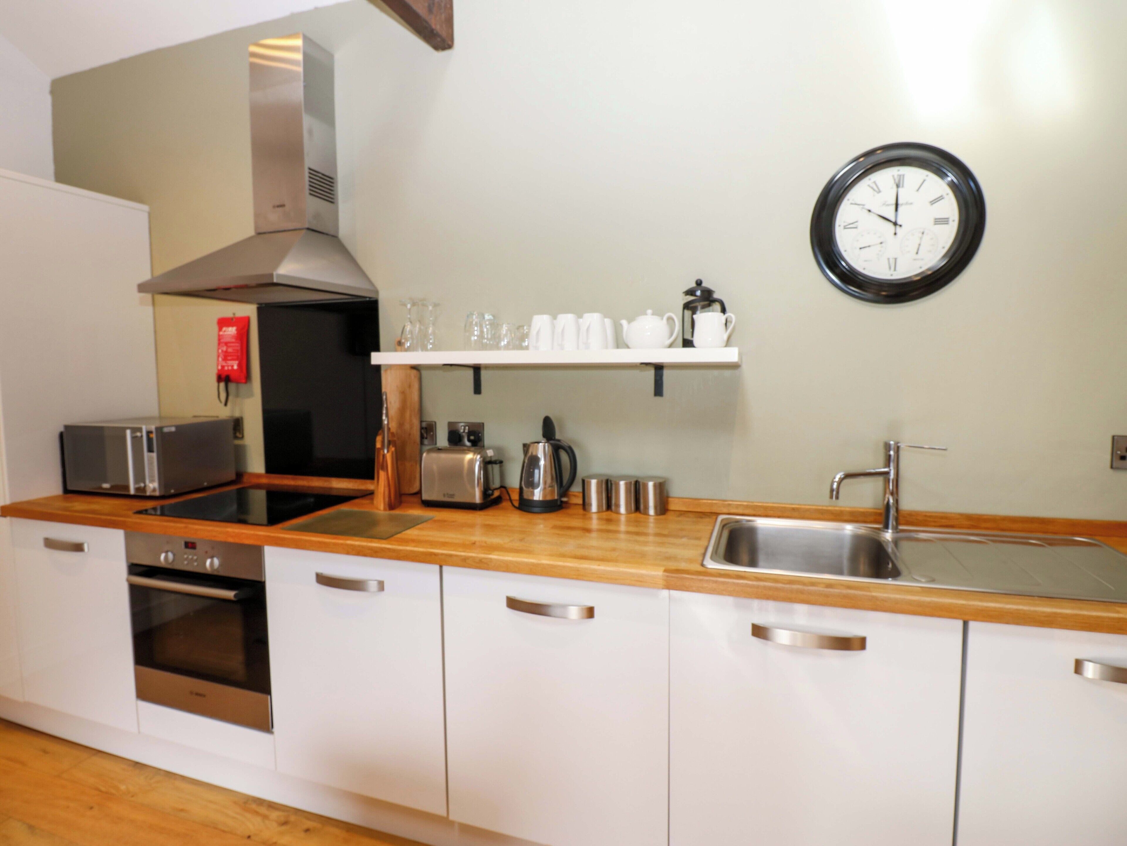 A modern kitchen with stainless steel appliances, a wooden countertop, and a wall-mounted clock.