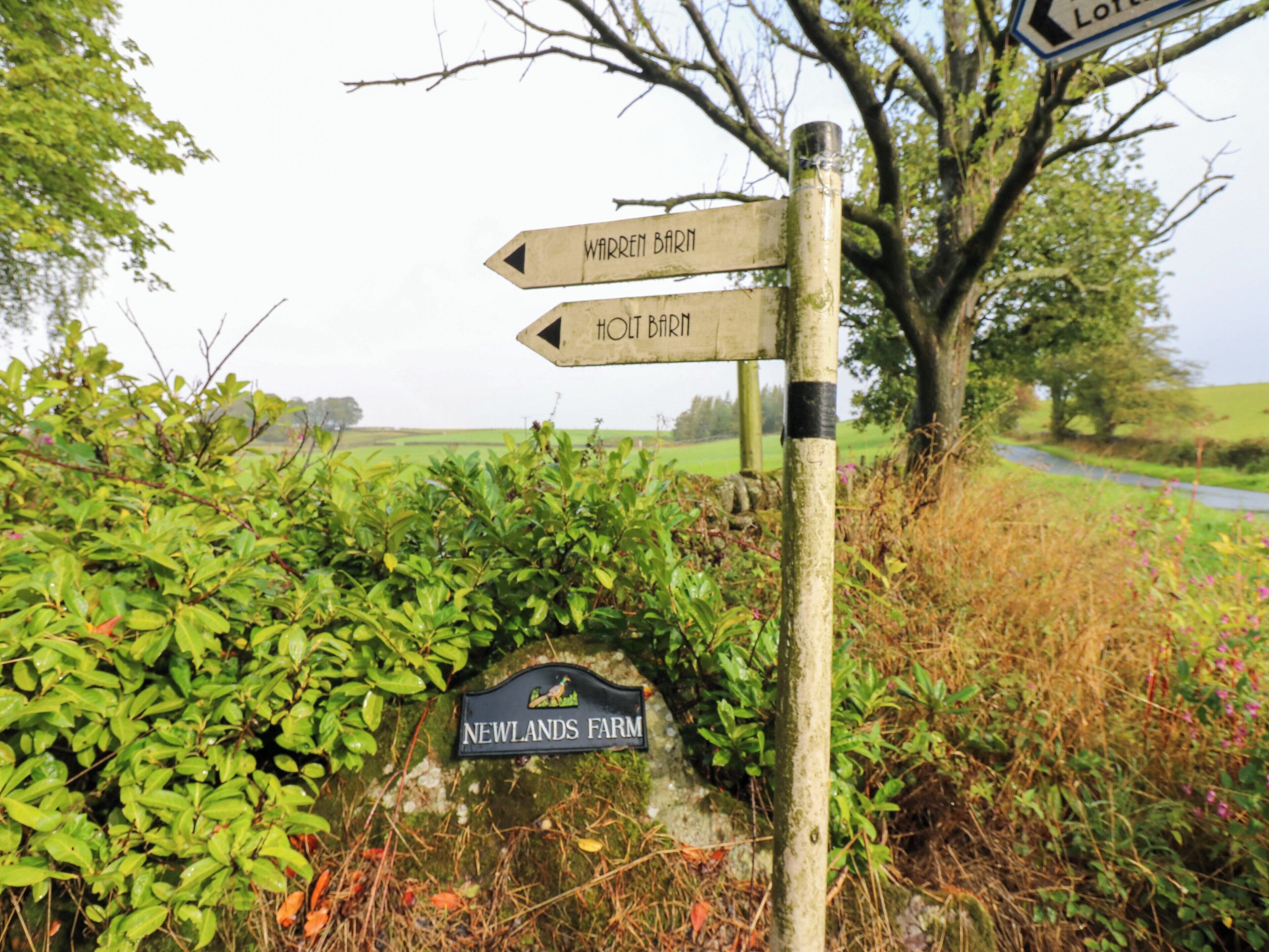 A directional signpost with arrows pointing to 'Warren Barn' and 'Holt Barn' with a 'Newlands Farm' sign below.