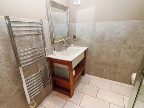 A bathroom with a chrome towel rack, a white sink, a mirror, and beige tiled walls and floor. - The Holt Barn (Ripon)