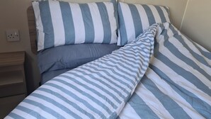 Una cama con ropa de cama a rayas, una mesita de noche y un enchufe de pared.