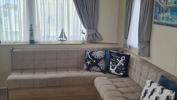 A living room with a large L-shaped sectional sofa, a ceiling fan, and a window with curtains.