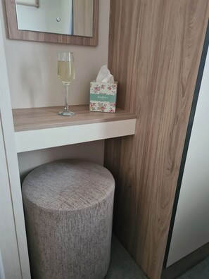 Une petite coiffeuse en bois, avec un miroir, une boîte de mouchoirs et un verre d’eau.