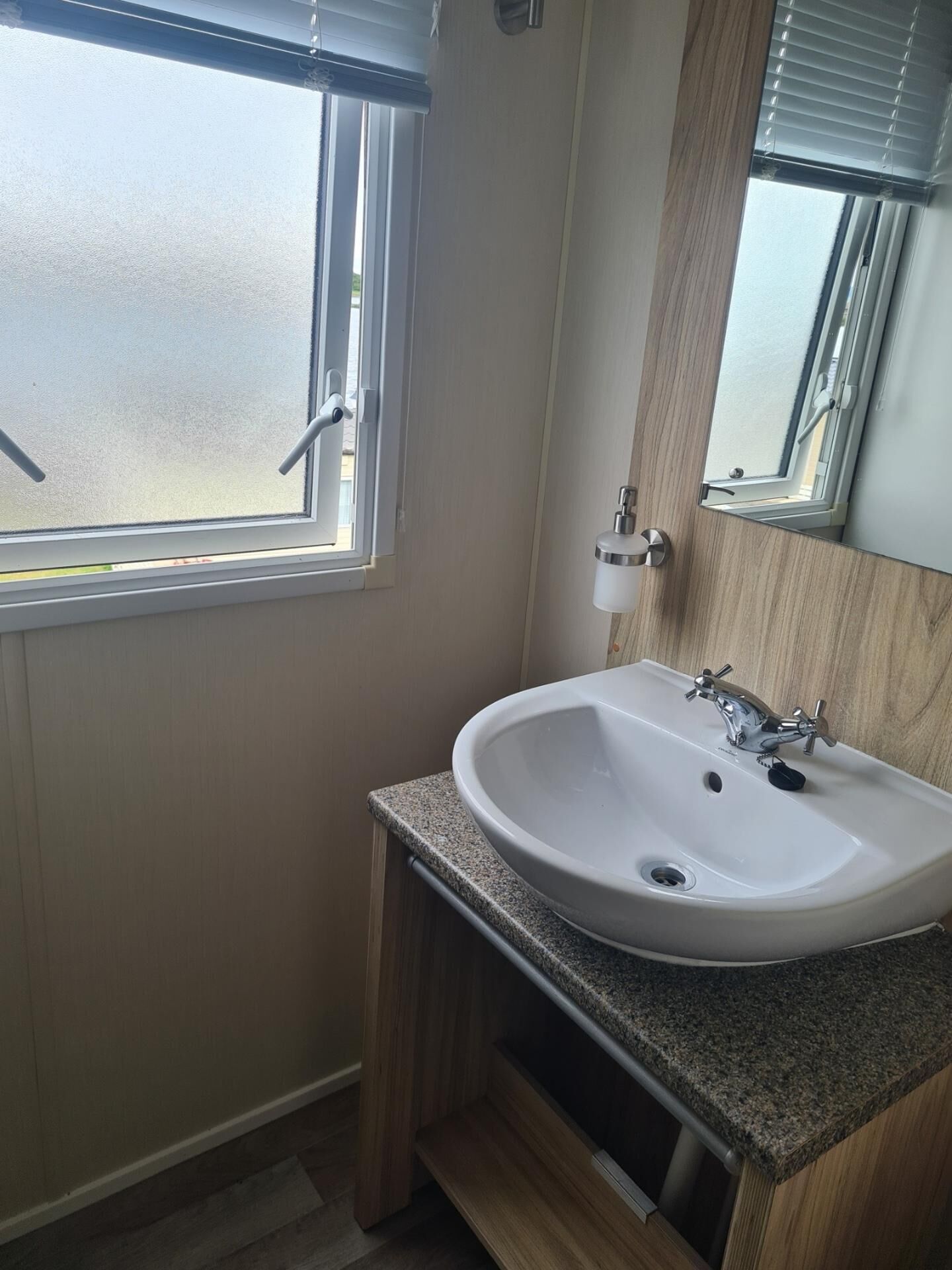 Ein Badezimmer mit weißem Waschbecken, Holzwaschtisch und einem Fenster mit Jalousien.