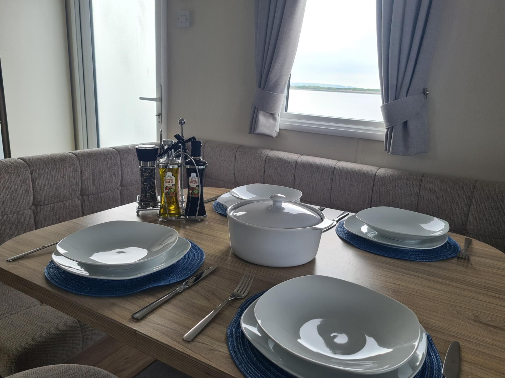 A dining area with a wooden table set for four, including plates, cutlery, and a large pot.