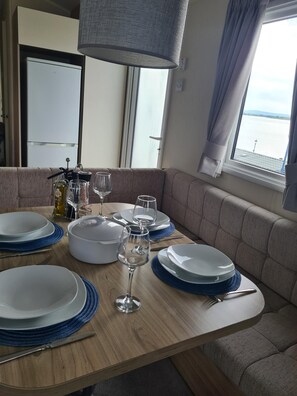 Un coin repas avec une table dressée pour quatre personnes, un canapé, une lampe et une vue sur l’eau.