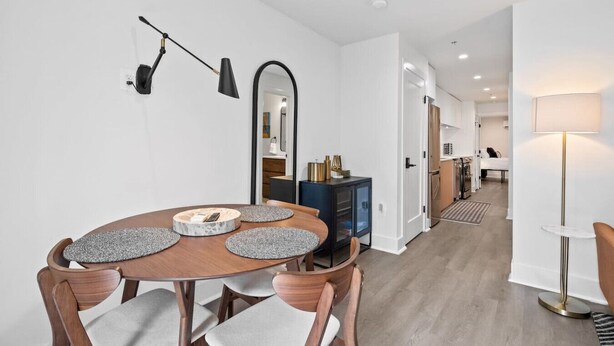 Een moderne eetruimte met een houten tafel en stoelen, een zwarte hanglamp en een spiegel aan de muur.
