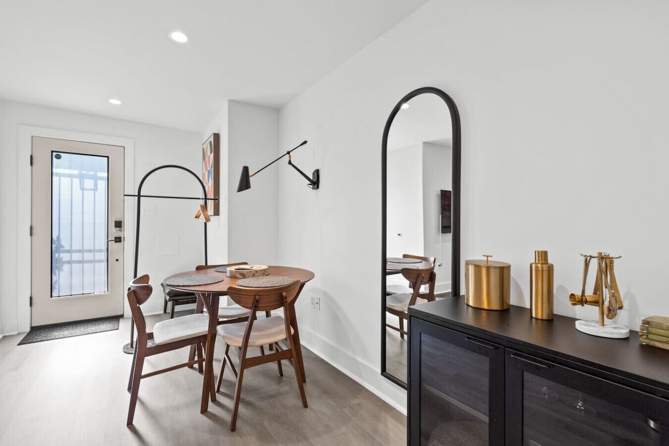 A modern dining area with a round table and chairs, a large mirror, and a black cabinet with decorative items.