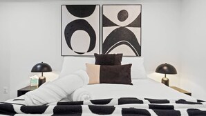 Een moderne slaapkamer met een bed, twee nachtkastjes, twee lampen en abstracte wanddecoratie.