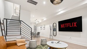 Ein modernes Wohnzimmer mit Treppe, Essbereich und einem großen Fernseher, der "NETFLIX" anzeigt.