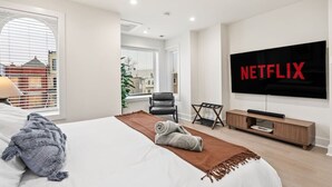 Ein modernes Hotelzimmer mit einem großen Bett, einem an der Wand montierten Fernseher und Blick auf die Stadt durch die Fenster.