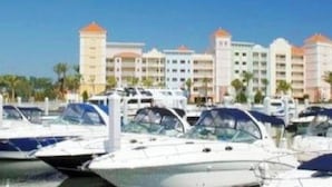 A marina with several boats docked, a hotel with multiple buildings in the background, and a clear blue sky.