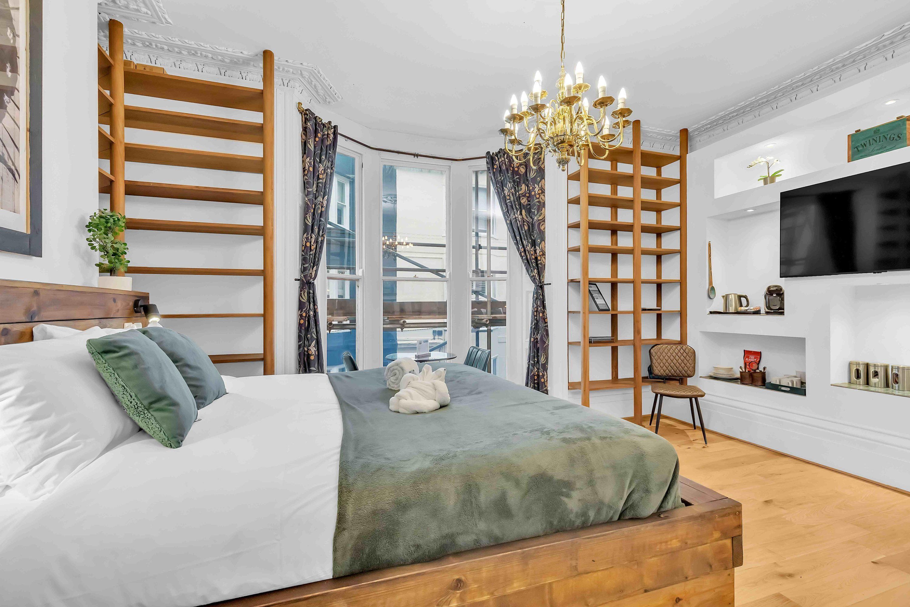 A modern bedroom with a large bed, wooden ladder, chandelier, and a TV mounted on the wall.