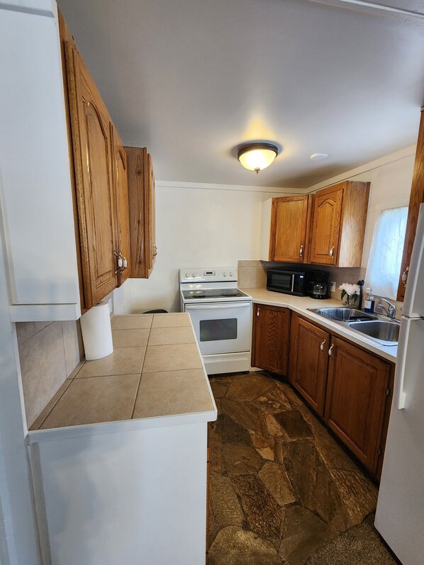 A compact kitchen with wooden cabinets, a white refrigerator, a stove, a microwave, and a sink. - Cozy peaceful home in Lehi (Lehi)
