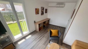 Een moderne woonkamer met houten vloer, een bank, een salontafel en een tv-meubel. Er staat een lange bank met stoelen, een kleine plant en kunst aan de muur.