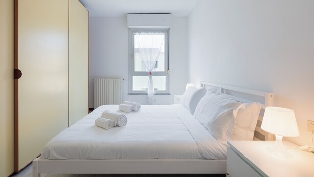Siisti hotellihuone, jossa on huolitellusti pedattu sänky, yöpöytä lampun kanssa ja ikkuna, jossa on verhot.