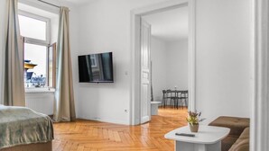 Een moderne woonkamer met een flatscreen televisie, een bank, een bijzettafeltje met een plant, en een eethoek op de achtergrond.