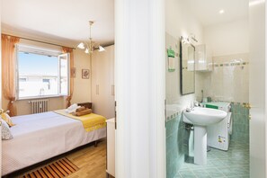 Un dormitorio con cama, ventana y baño con lavamanos y espejo.