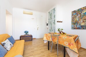A dining area with a table set for four, a sofa, a small side table with a vase, and a door leading to another room. - Bright 'Sunflower' Apartment with Wi-Fi (Roma)