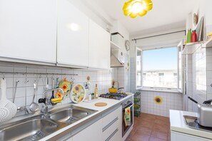 A kitchen with white cabinets, a gas stove, a sink, and a window with a view of buildings. - Bright 'Sunflower' Apartment with Wi-Fi (Roma)