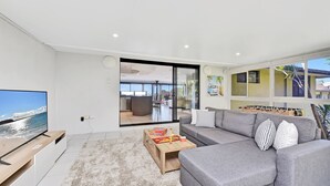 A modern living room with a grey sofa, a flat-screen TV, and a wooden coffee table. - Oasis at Salamander Bay (Salamander Bay)
