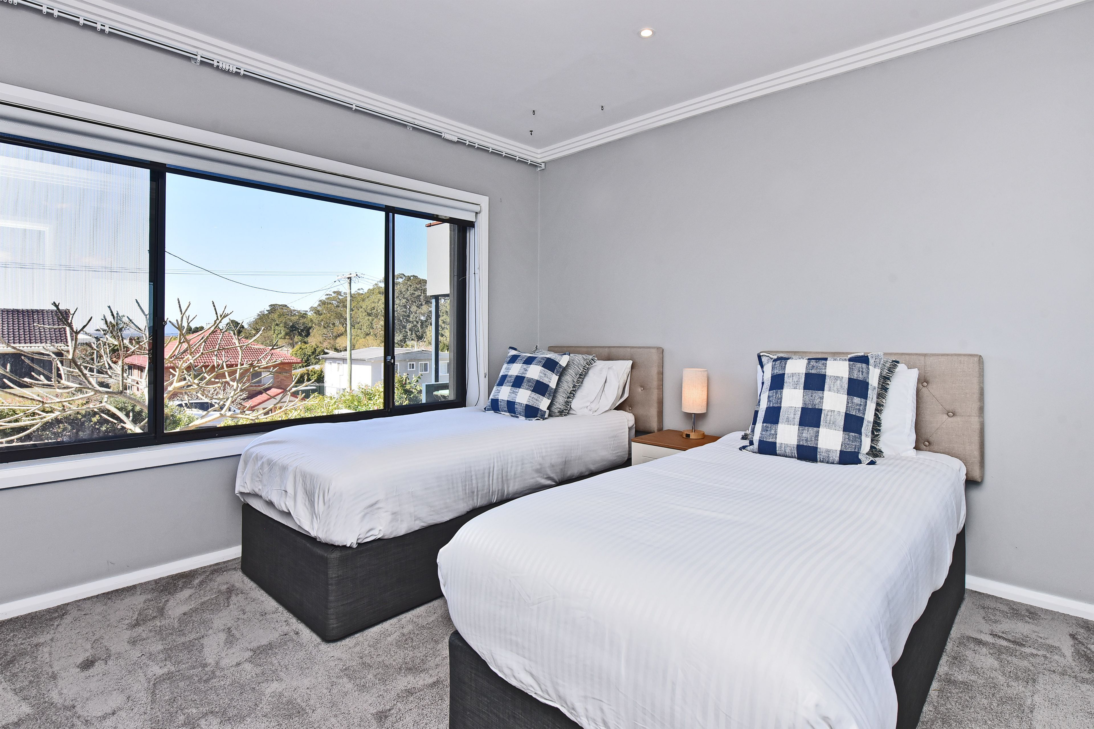 A bedroom with two beds, a large window, and a view of buildings outside.